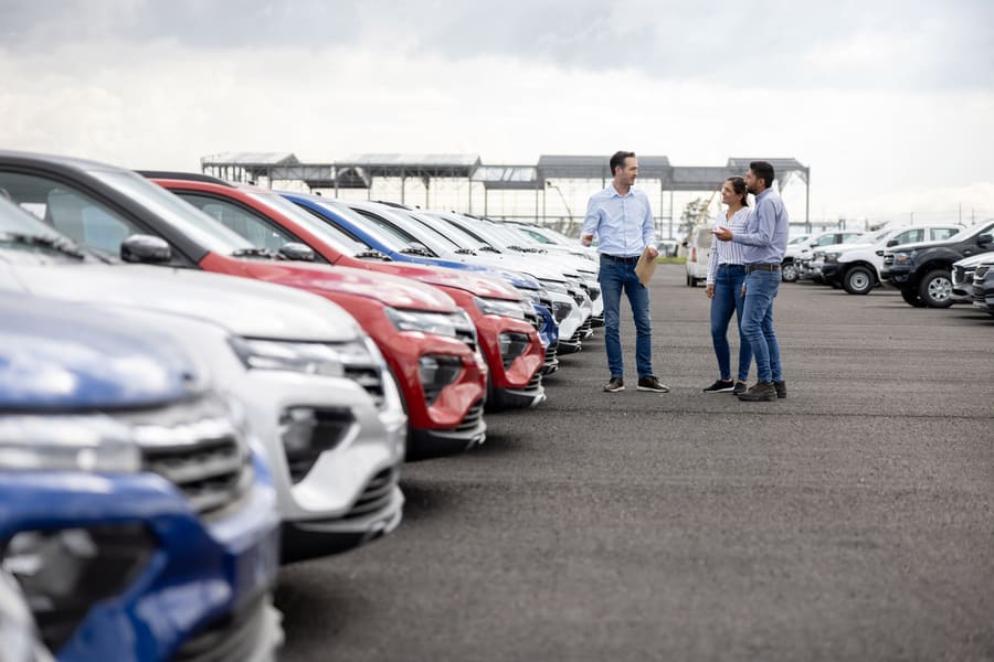 A row of cars on a forecourt, with a salesperson talking to two buyers